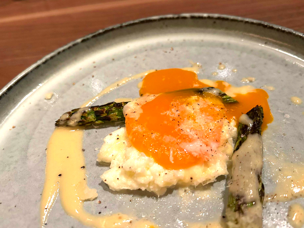 イタリアの定番料理である、炭火焼にしたアスパラに卵を取り合わせた“アスパラ グラナパダーノ 卵”。シンプルな調理法ゆえに、素材力、そして火入れのセンスが問われる一品だ（画像は火入れ具合を写すために筆者が黄身を割ったもの）