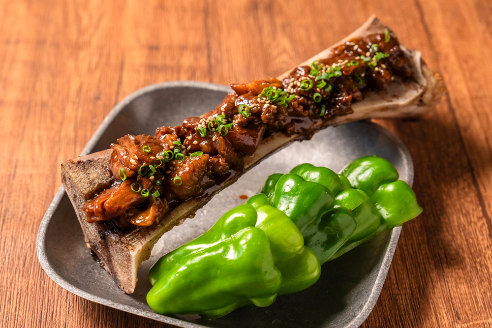 パリパリピーマンでドテ煮を食べる‟渋谷のパリピ”。なんと!トロトロになるまで脊髄を煮込んだ牛骨を縦割りにし、その上にドテ煮がかかっているダイナミックな一皿。その美味しさを、ネーミングの面白さと共に味わってもらいたい