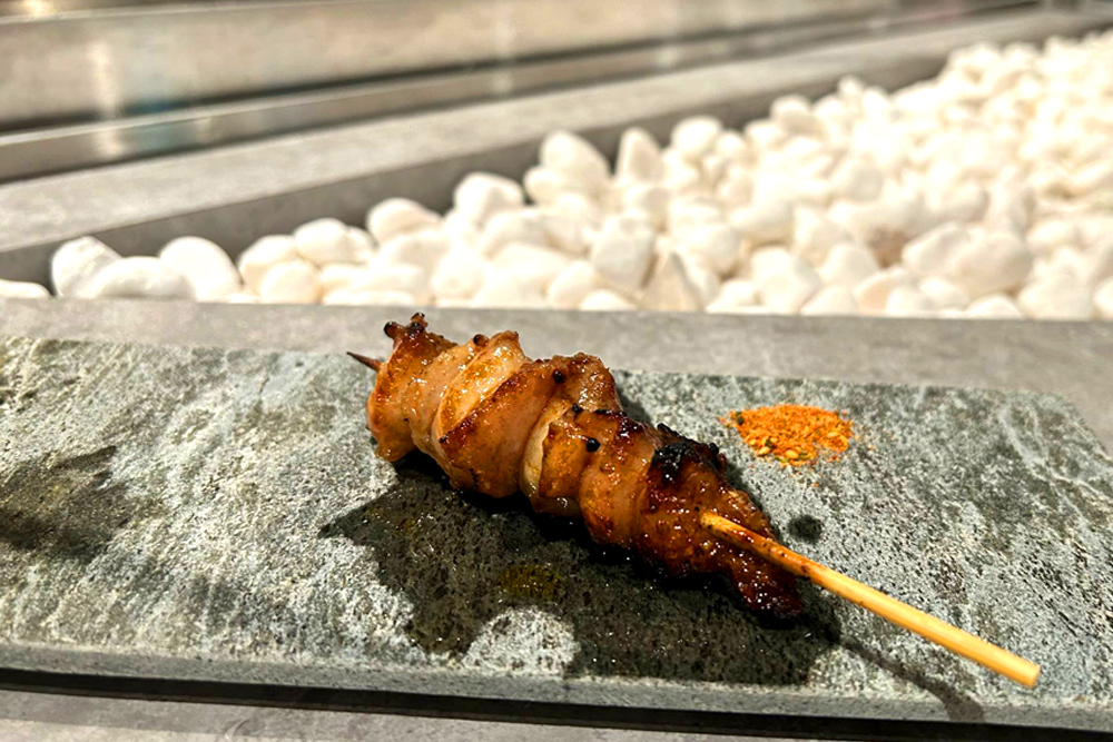 白石をバックにした‟ぼんじり“。タレを塗って焼かれたこの一本は、料理長特製のブレンドスパイスと共に食すのがおススメだ