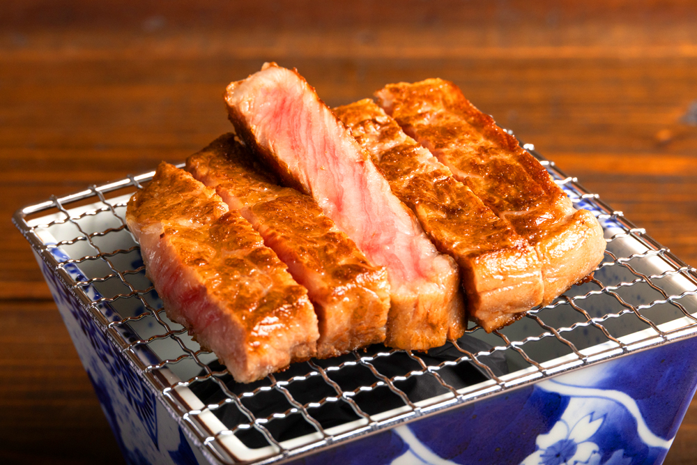 “宮崎牛サーロインステーキ”。 料理人がオープンキッチンで生肉からカットし、焼き、焼き上がった後に再度カットして、七輪にのせたスタイルで提供される。香ばしさと肉の旨みが引き立つ、贅沢な一品だ