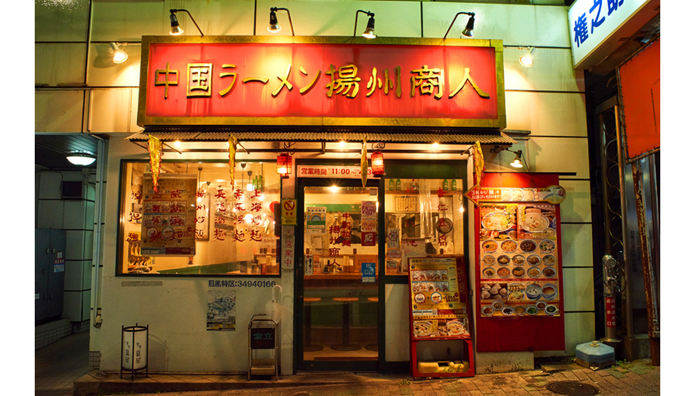 「揚州商人」第一号店であり、目黒本店の外観。全店舗に共通する印象的なデザインは、“「揚州商人」といえば！”という存在感を放つ。また、多岐に渡る味の組み合わせも、直営店はもちろんのことフランチャイズ店でも標準化されるよう、セントラルキッチンと‟100本を超えるレードル“を用いた独自オペレーションで実現している