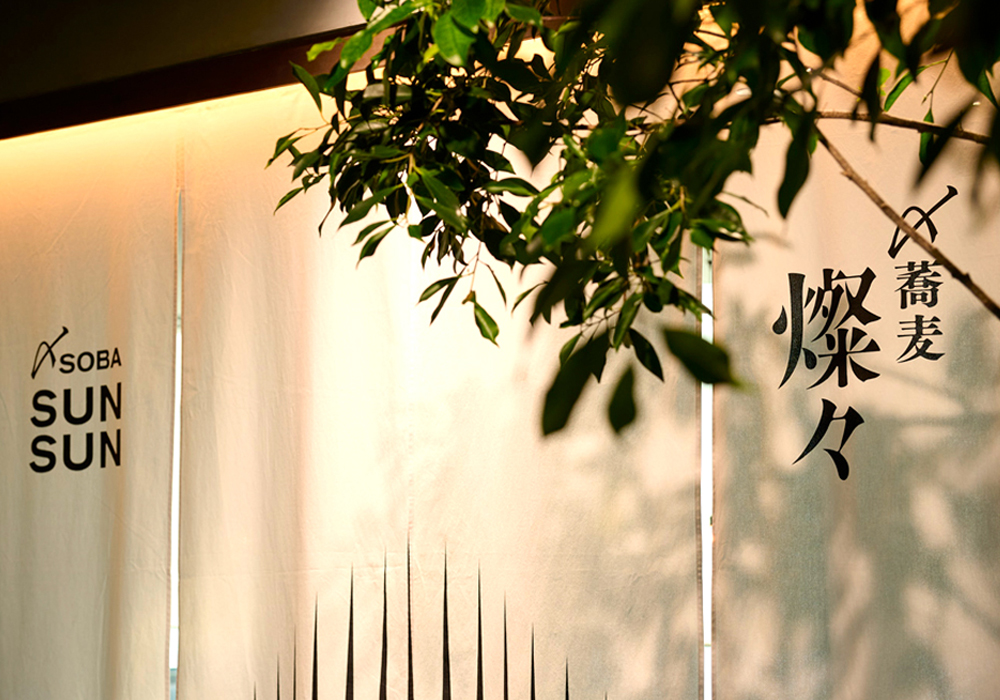 店舗外観。都心の高層ビルにいることを忘れさせる緑あふれる環境の中で、日本人には親しみやすく、インバウンドにはノスタルジックな空間で、現代的なアプローチを取り入れた蕎麦文化を堪能できる店が誕生した