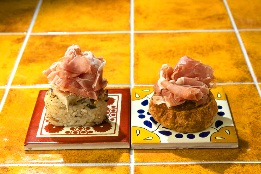 炊き込みご飯の旨みに、トリュフの香りとハモンのコクを加えた贅沢な味わいの‟炊き込みご飯おにぎり ハモン＆トリュフソース添え（画像左）”と、卵のやさしい味わいにハモンの旨みを重ねた‟卵焼き ハモン添え（画像右）“。どちらもCAVAとの相性が抜群であり、和とスパニッシュのペアリングの極意を味わえる逸品だといっていい