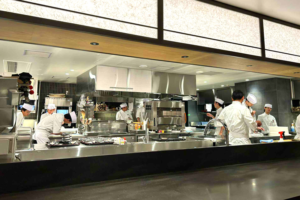 満席時には220名のお客さまを迎え入れるオープンキッチン。規模の大きさに加え、エントランスから個室への導線越しに調理の光景を望むことができ、ライブ感あふれる空間となっている