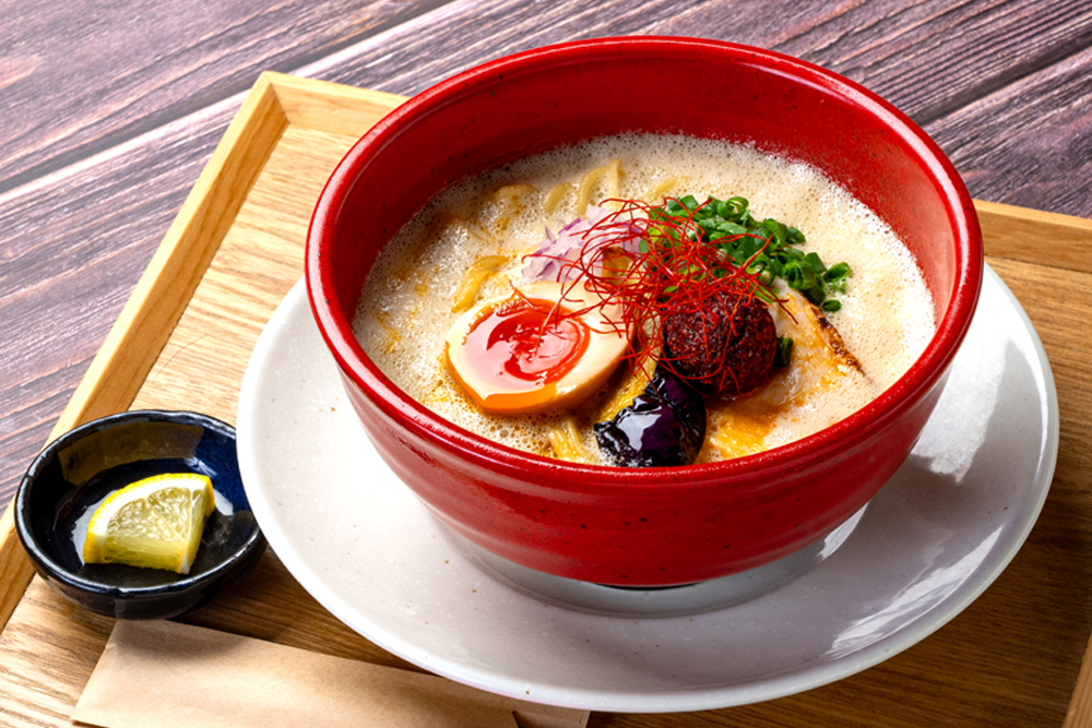 「白鶏舎」の“辛味噌鶏白湯”。同店のすべてのラーメン(※「トリノイロ」で提供するミニラーメンを含む)に、味変用として黒胡椒、りんご酢、カットレモンが添えられる。それぞれが鶏と豚骨の旨味を引き立てる要素となるが、なかでもフレッシュレモンのさわやかさが、味わいに意外性のある広がりをもたらす